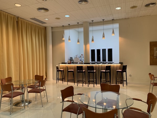 A modern hotel lobby with a glass table and chairs, a reception desk, and pendant lighting.