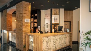Mostrador de recepción con una encimera de madera y un cartel que indica la hora del café. Se observa una pared de ladrillo al fondo del mostrador y una planta a la izquierda.