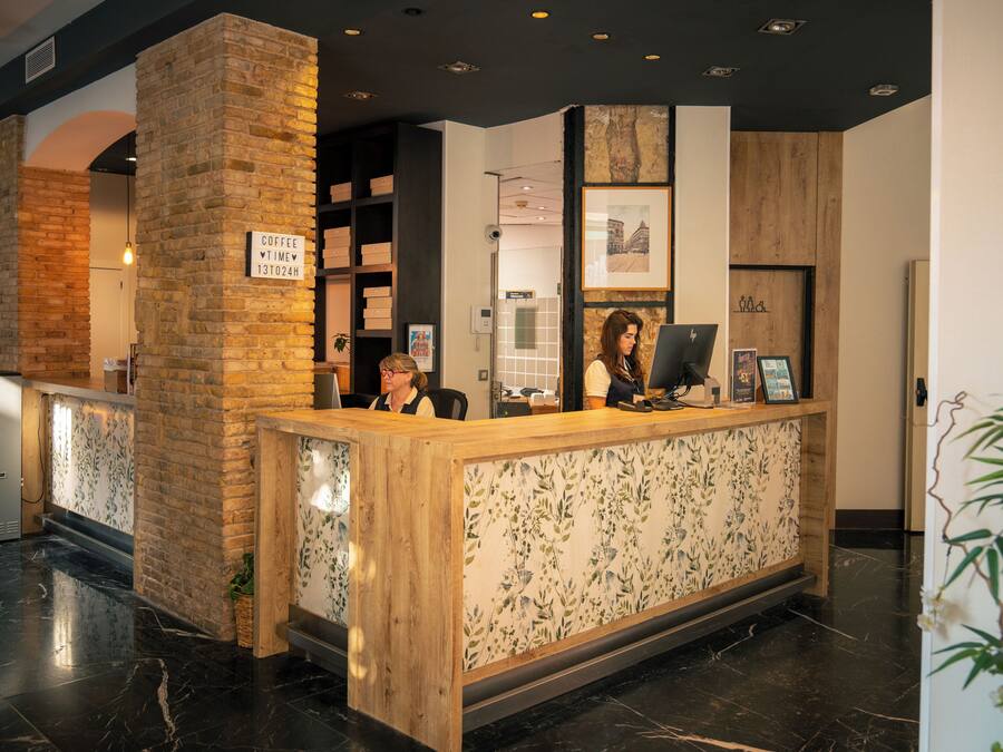 A reception desk with a wooden counter and a sign indicating coffee time. There is a brick wall behind the desk and a plant to the left.