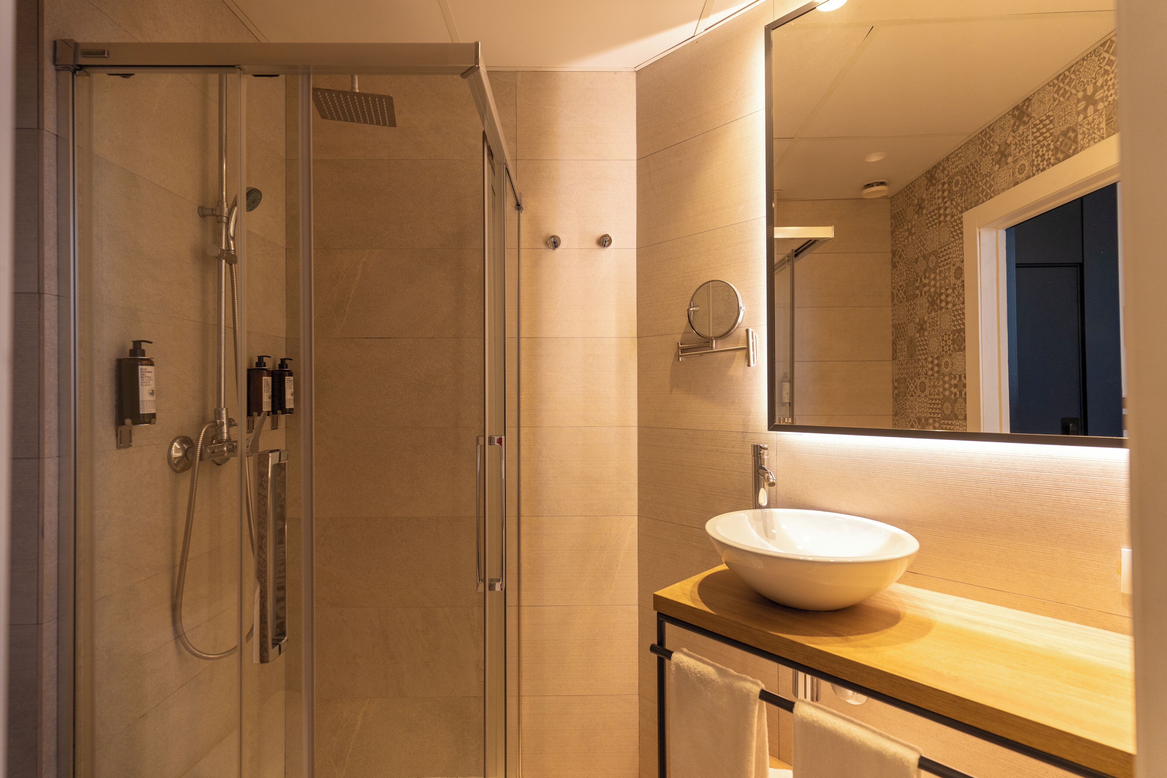 A modern bathroom with a glass-enclosed shower, a large mirror, and a wooden vanity with a white sink.