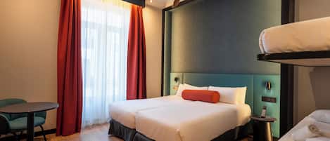 A hotel room with a bed, a desk, a chair, a ceiling fan, and a window with curtains.