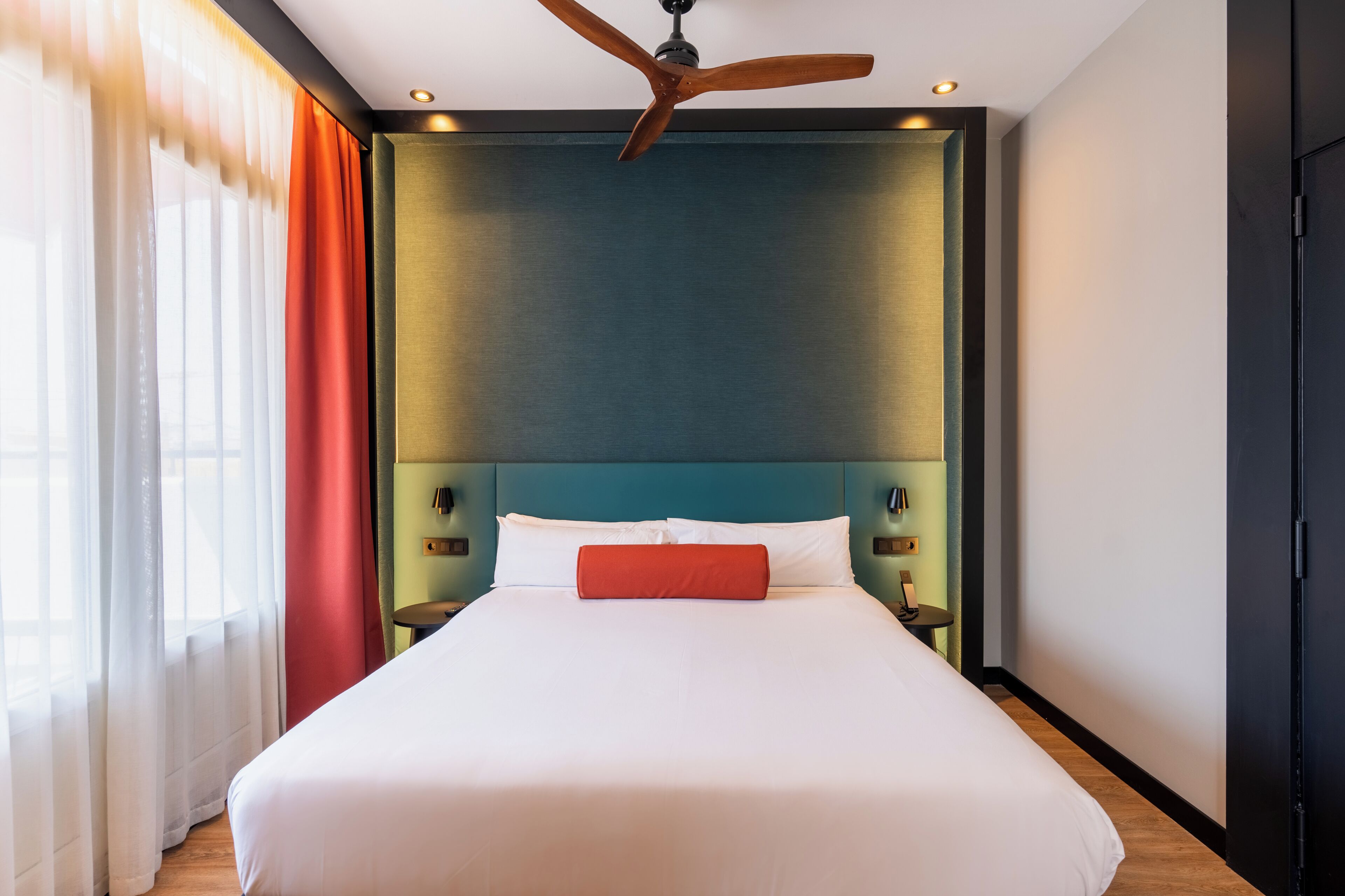 Ein Hotelzimmer mit einem großen Bett, einem Deckenventilator und Blick ins Freie durch das Fenster.