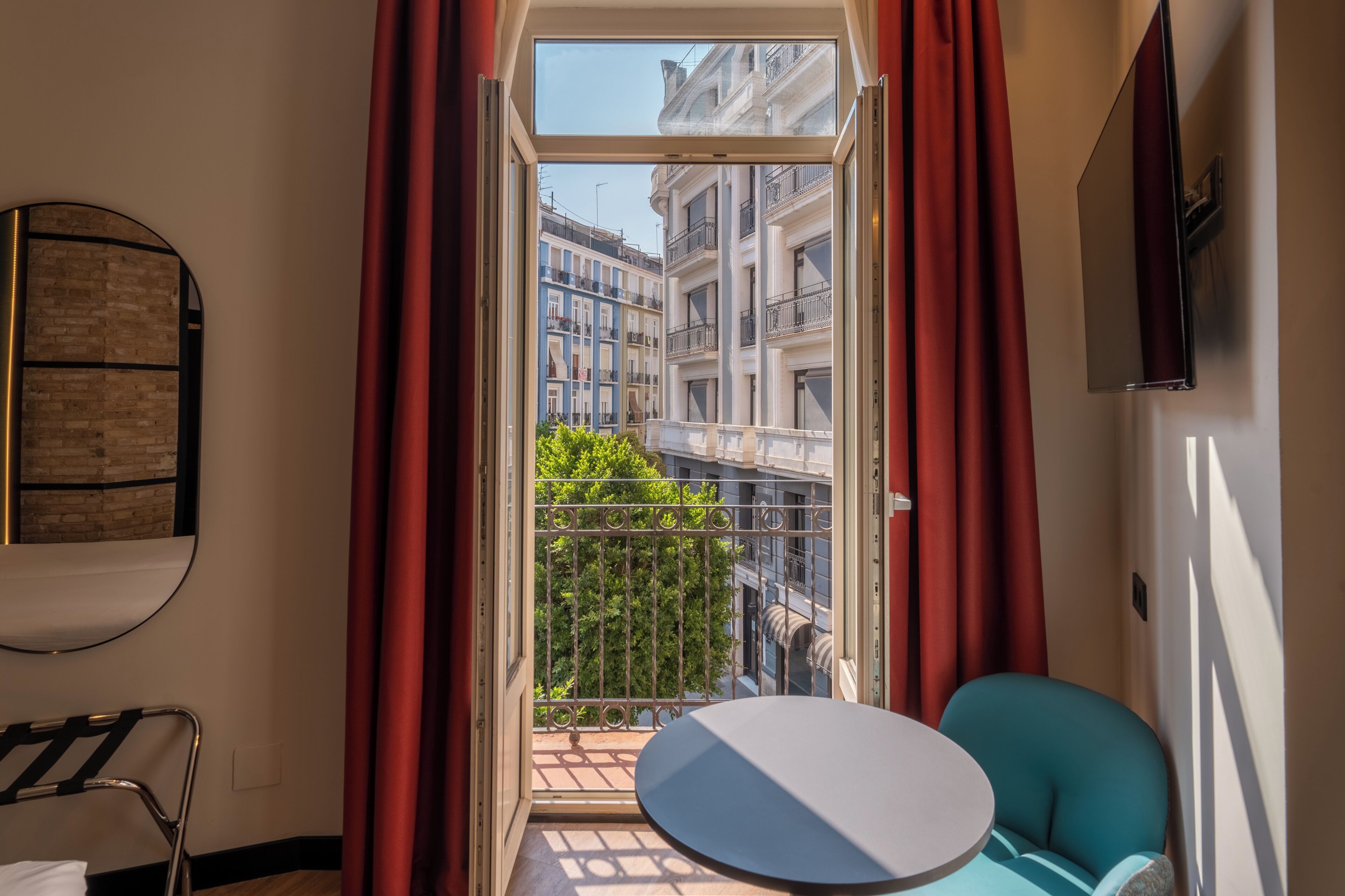 A room with a balcony, a round table, a chair, and a view of buildings.
