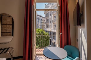 A room with a balcony, a round table, a chair, and a view of buildings.