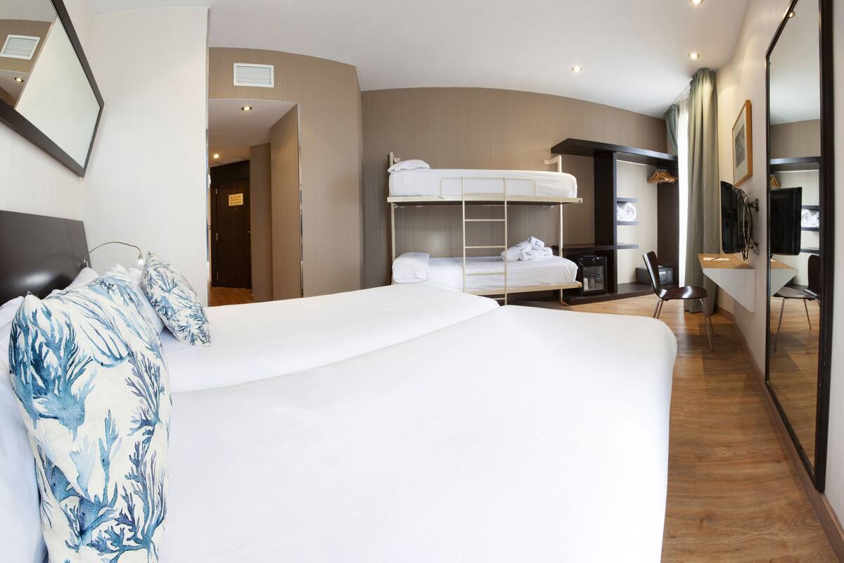 A hotel room with a bunk bed, a desk, a chair, and a large mirror.