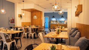 A restaurant interior with wooden tables and chairs, pendant lighting, and a kitchen area in the background.
