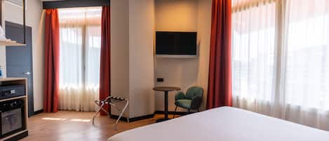 Une chambre d’hôtel avec un grand lit, un téléviseur fixé au mur, une petite table avec une chaise et un mini-bar.