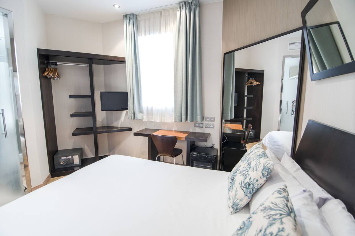 A hotel room with a bed, a desk, a chair, a TV, a wardrobe, and a mirror.