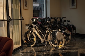 A row of bicycles parked indoors, with a glass door and a chair visible in the foreground. - Petit Palace Ruzafa Hotel (Valencia)