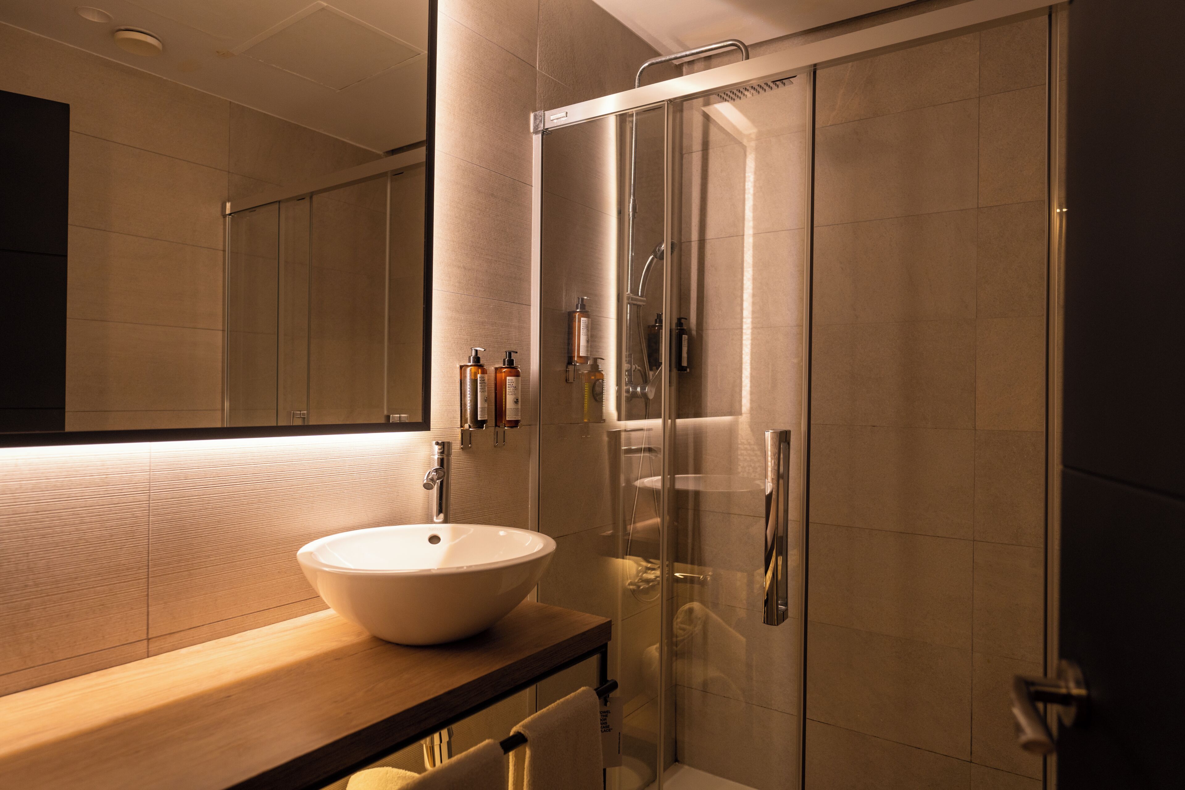 Un baño moderno con un espejo grande, un lavabo redondo y una ducha con cerramiento de vidrio.