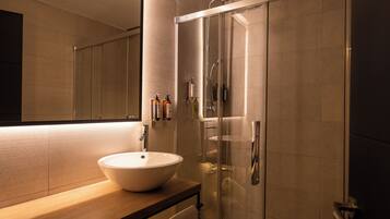 Un baño moderno con un espejo grande, un lavabo redondo y una ducha con cerramiento de vidrio.