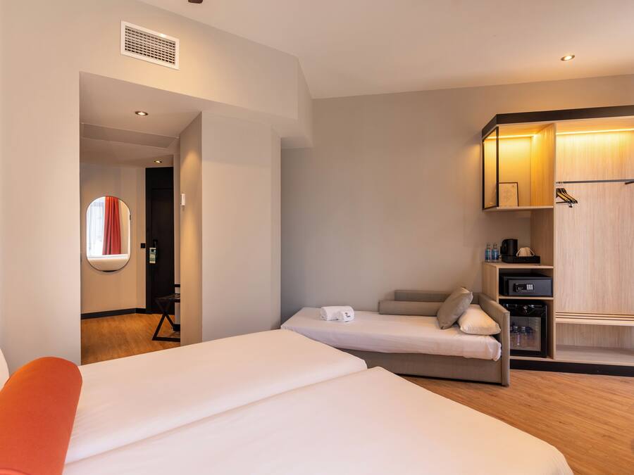 Habitación de hotel con una cama grande, una cama más pequeña, zona de estar, armario y espejo.