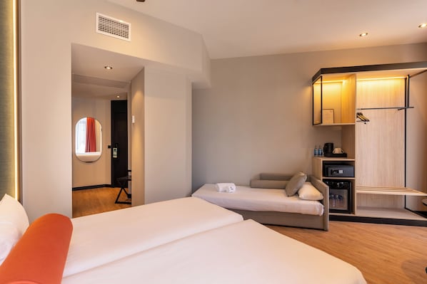 A hotel room with a large bed, a smaller bed, a seating area, a wardrobe, and a mirror.