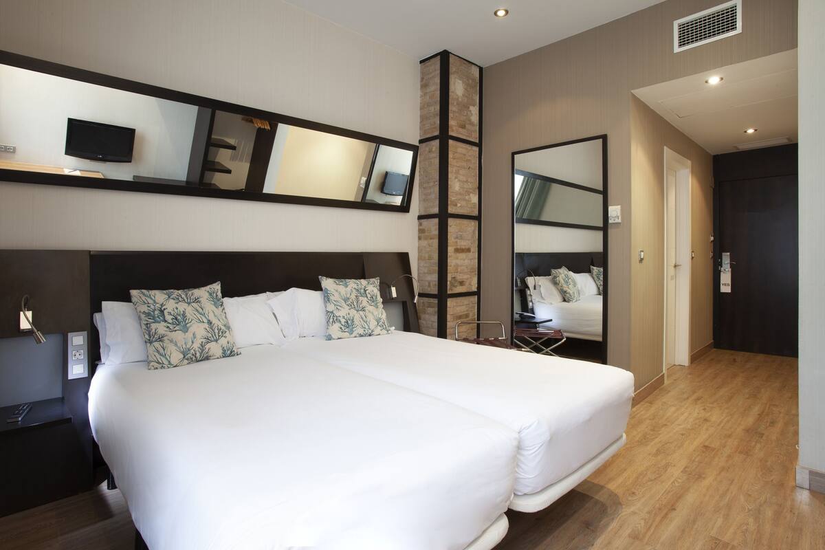 A modern hotel room with a large bed, a TV, and a mirror.