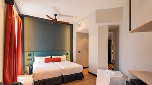 A hotel room with a bed, a desk, a chair, a ceiling fan, and a view of the hallway.