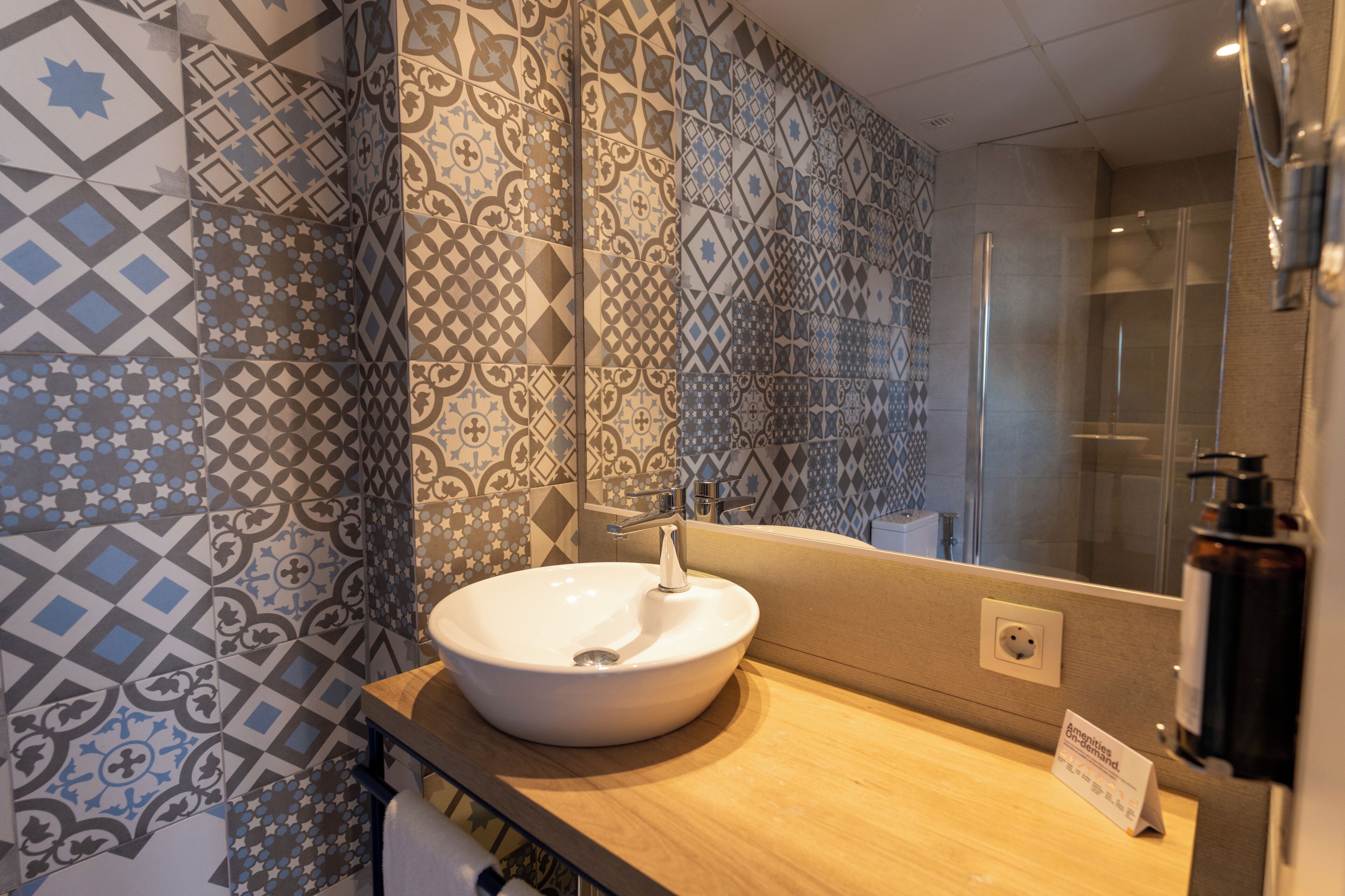 A bathroom with a white sink, a mirror, and patterned tiles on the walls.