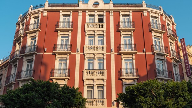 A multi-story building with a red facade, multiple balconies, and a central entrance.