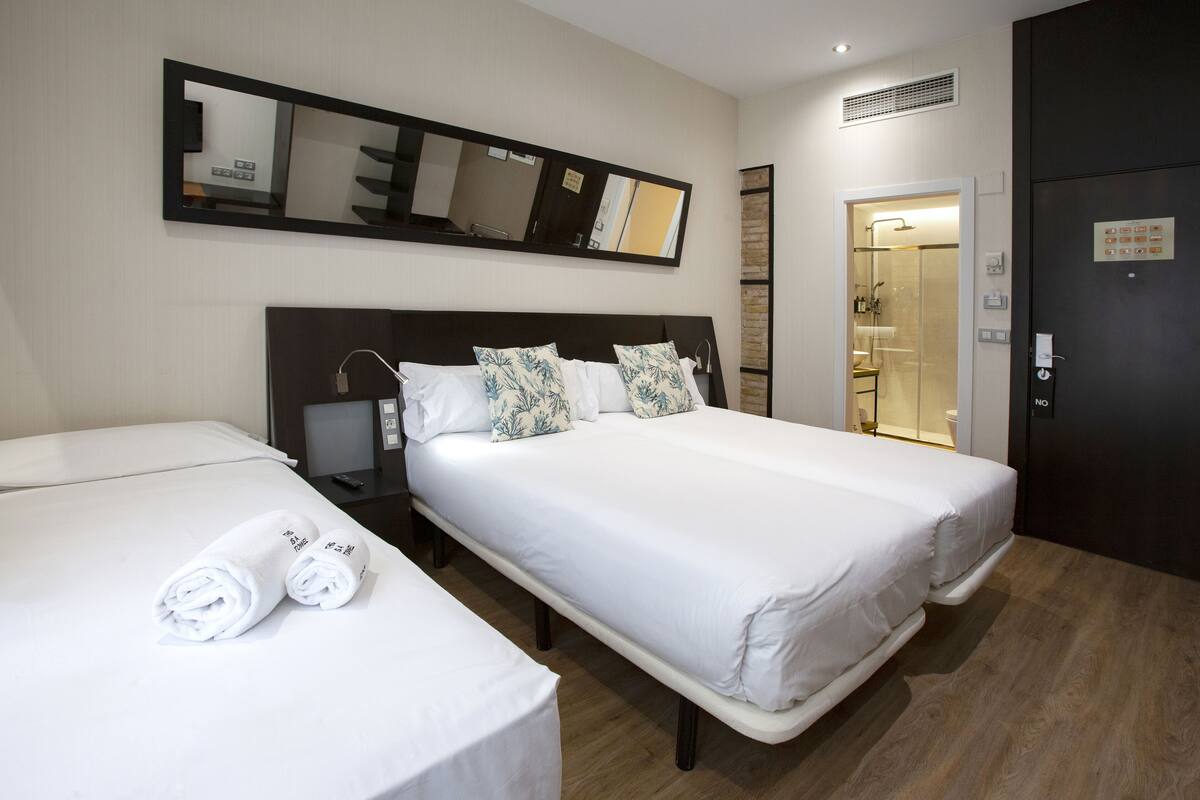 A hotel room with two beds, a large mirror, a nightstand, and a door leading to a bathroom.