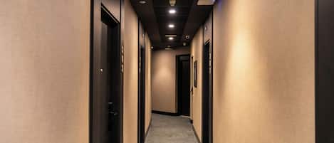 A hotel hallway with carpeted floors, doors on both sides, and recessed lighting on the ceiling.