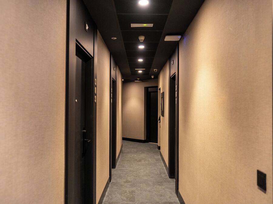 Un pasillo de hotel con pisos alfombrados, puertas a ambos lados e iluminación empotrada en el techo.