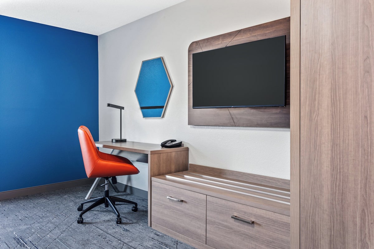 A modern office space with a blue accent wall, a wooden desk, an orange office chair, a black telephone, and a mounted flat-screen TV.