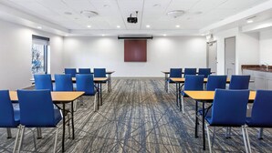 A conference room with blue chairs and tables, a projector screen, and a carpeted floor.