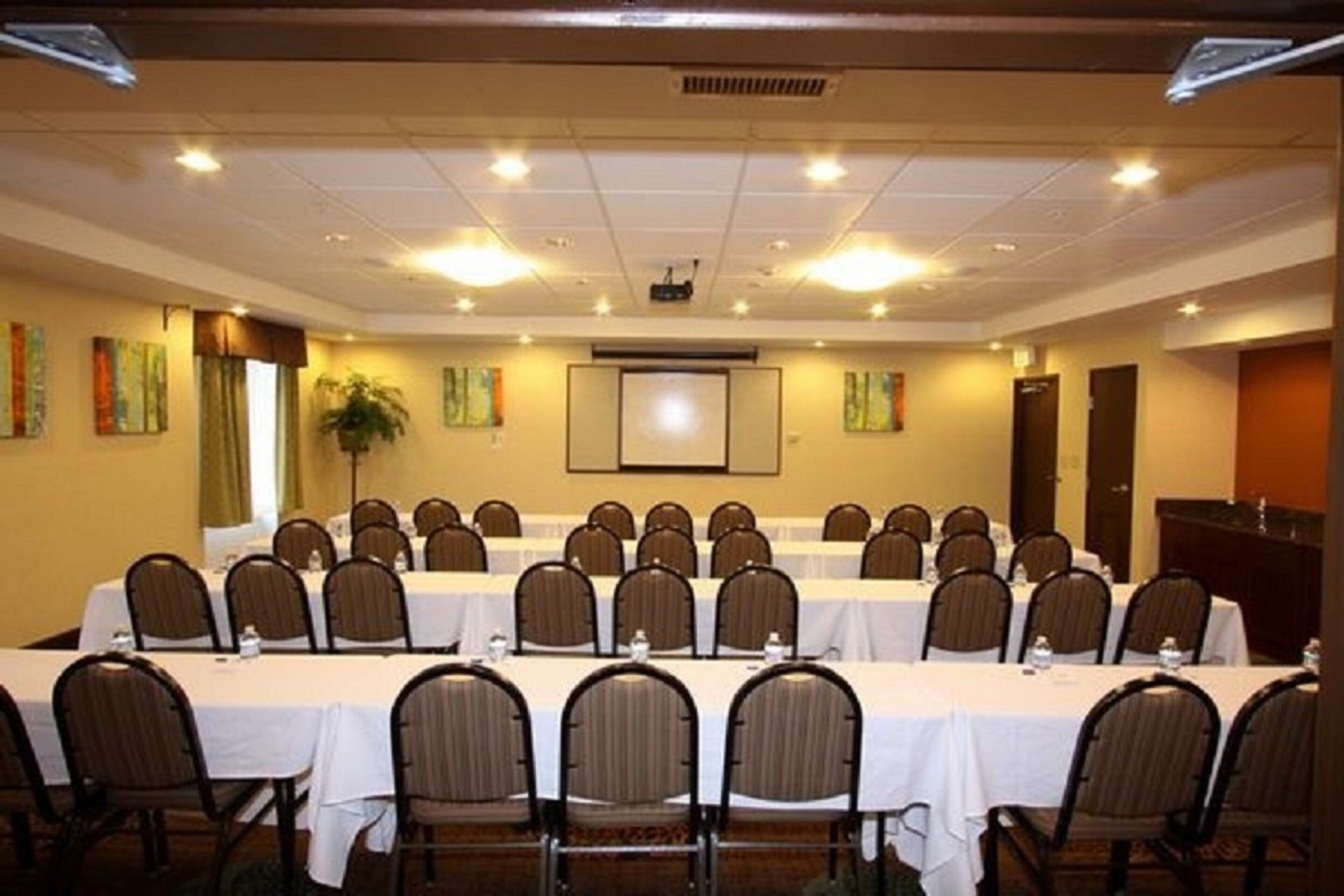 A conference room with multiple tables and chairs, a projector screen, and artwork on the walls.