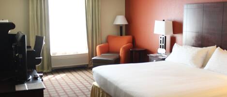 A hotel room with a large bed, a desk, a chair, and a television.