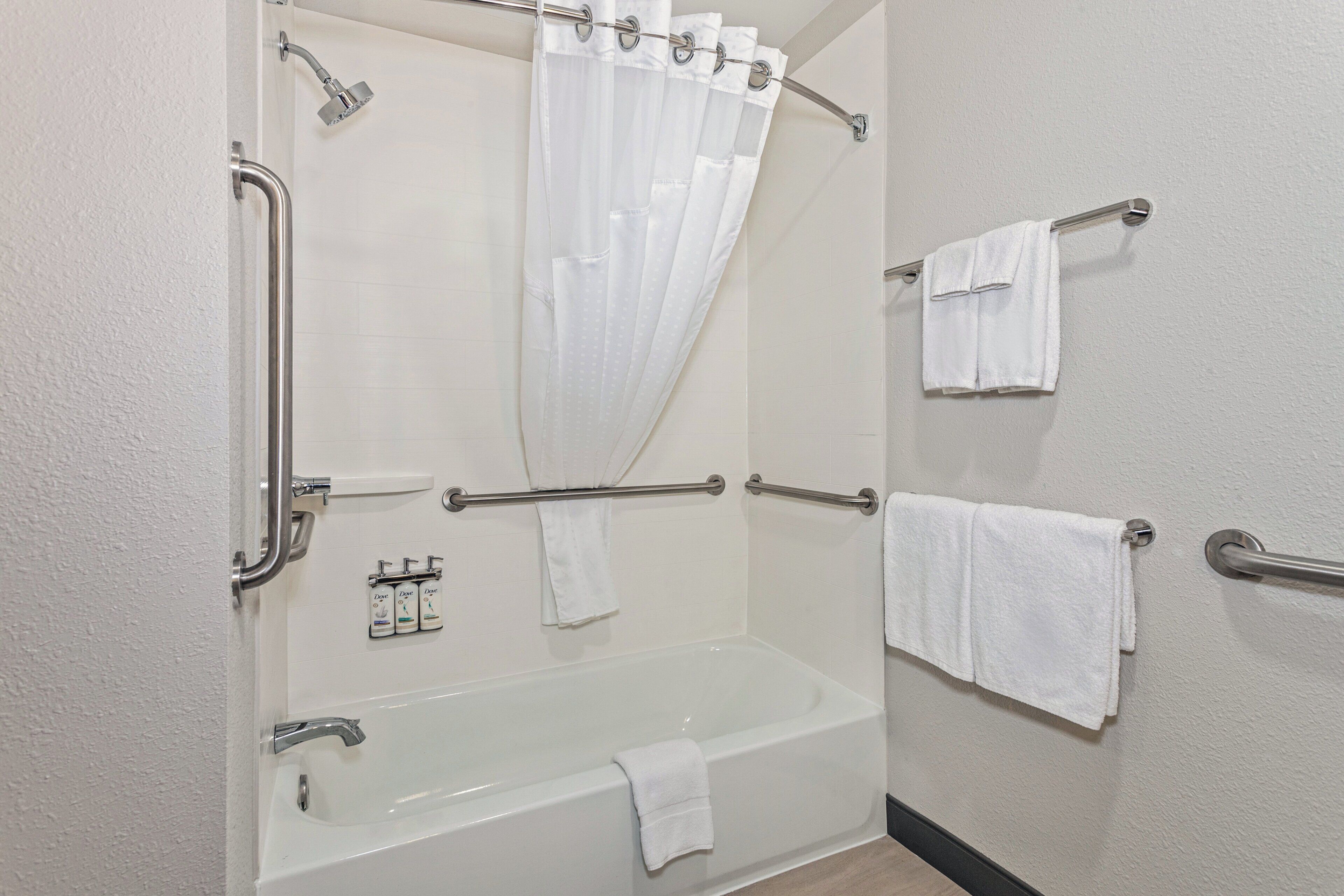 Une salle de bain équipée d’une baignoire, d’une douche avec rideau, de barres d’appui et de plusieurs serviettes.