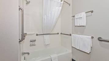 Une salle de bain équipée d’une baignoire, d’une douche avec rideau, de barres d’appui et de plusieurs serviettes.