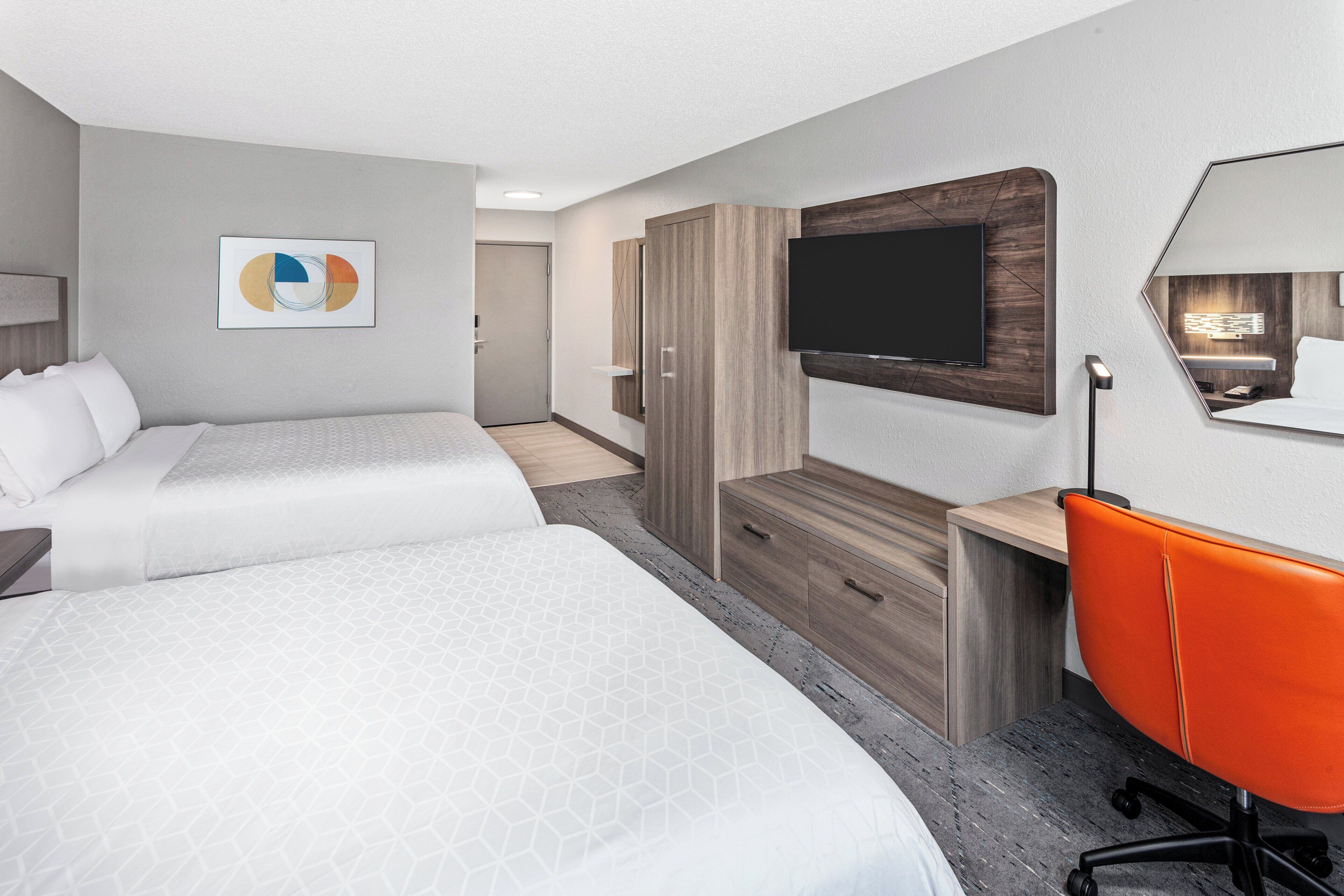 A hotel room with two beds, a desk, a chair, a TV, and a painting on the wall.