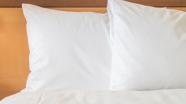 A bed with white bedding and pillows against a wooden headboard.