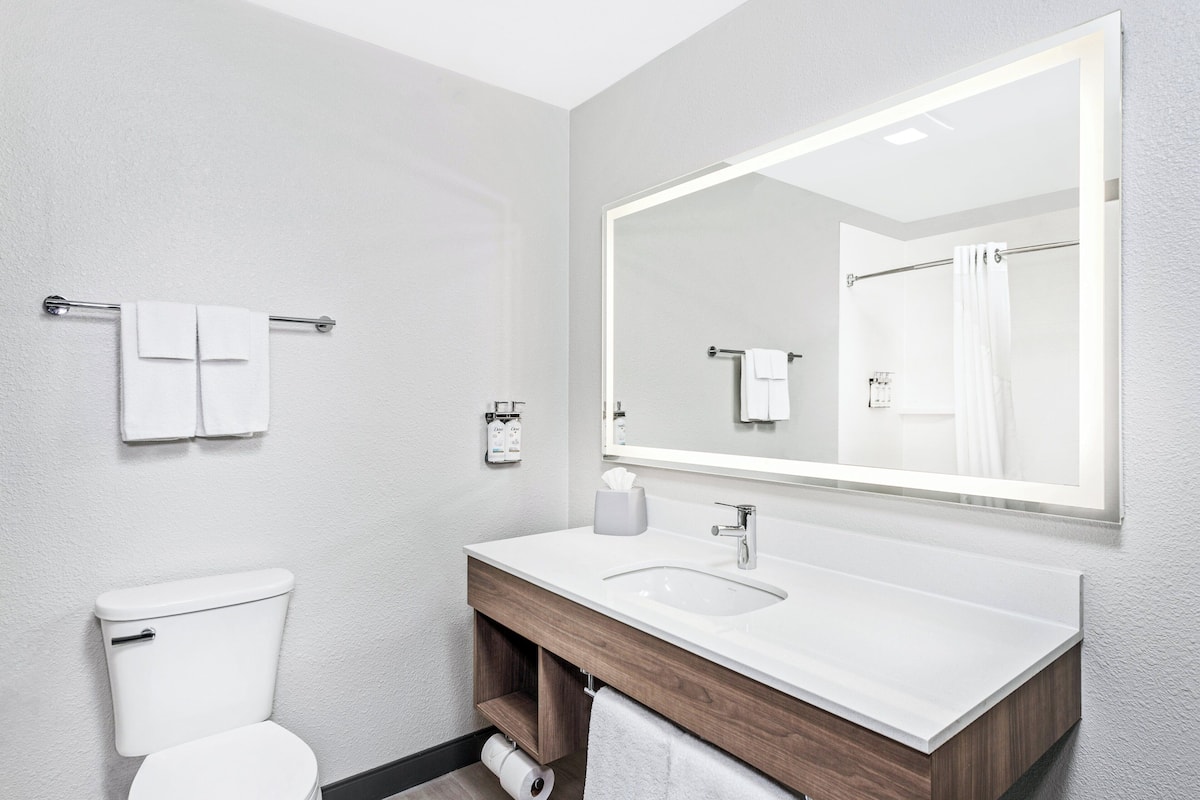 A modern bathroom with a white toilet, a large mirror, and a white sink with a wooden vanity.
