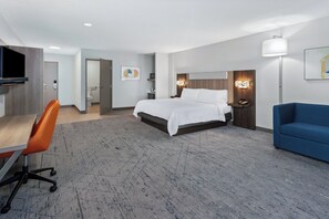 A hotel room with a bed, a desk with a chair, a blue sofa, and a television. - Holiday Inn Express Hotel & Suites Chicago-Algonquin by IHG (Algonquin)