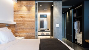 Une chambre d’hôtel moderne avec un mur d’accent en bois, un grand lit, un dressing et une salle de bain équipée d’un miroir et d’un lavabo.