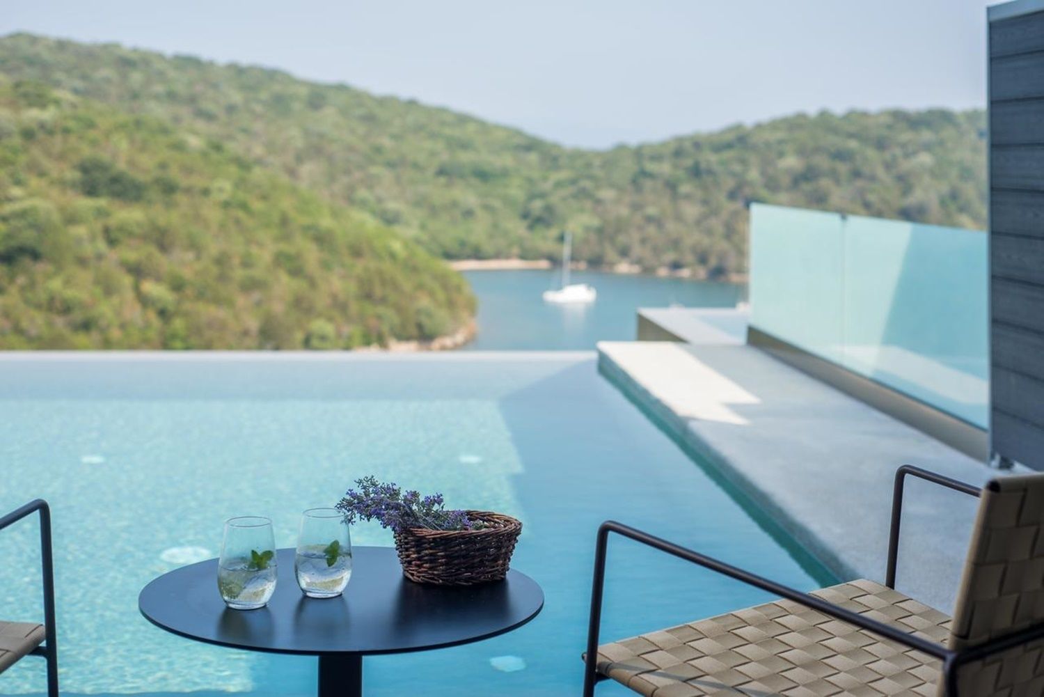 Vista da piscina com uma mesa, cadeiras e um cesto de vime com flores.