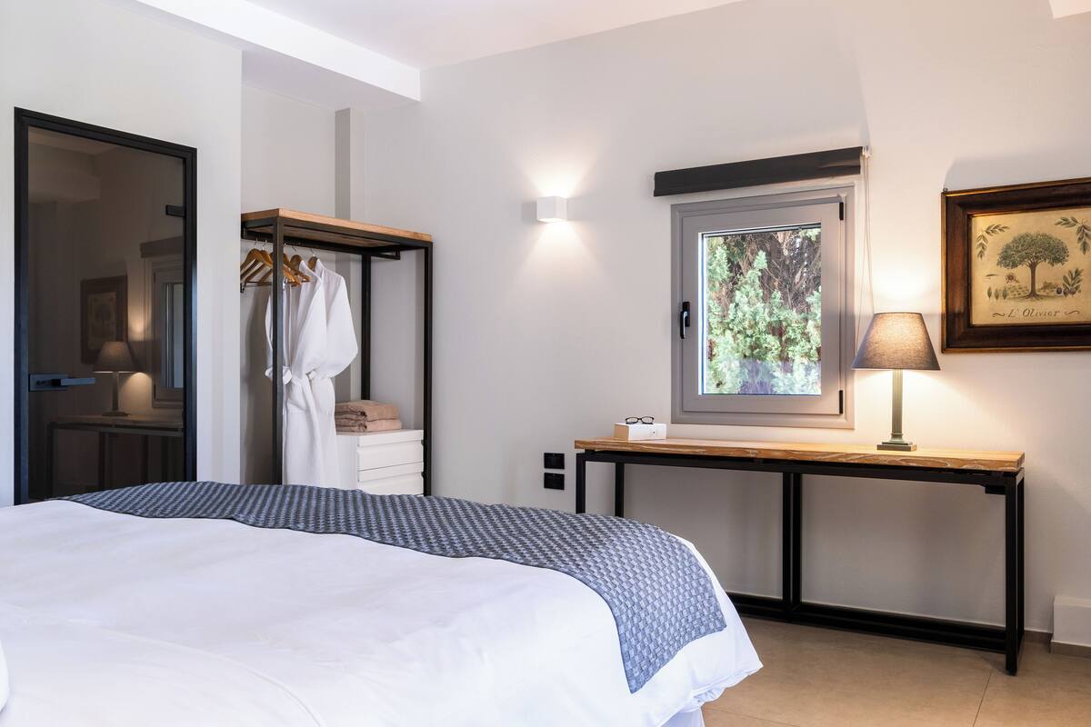 Een slaapkamer met een bed, een kledingkast, een bureau en een raam met uitzicht op bomen.