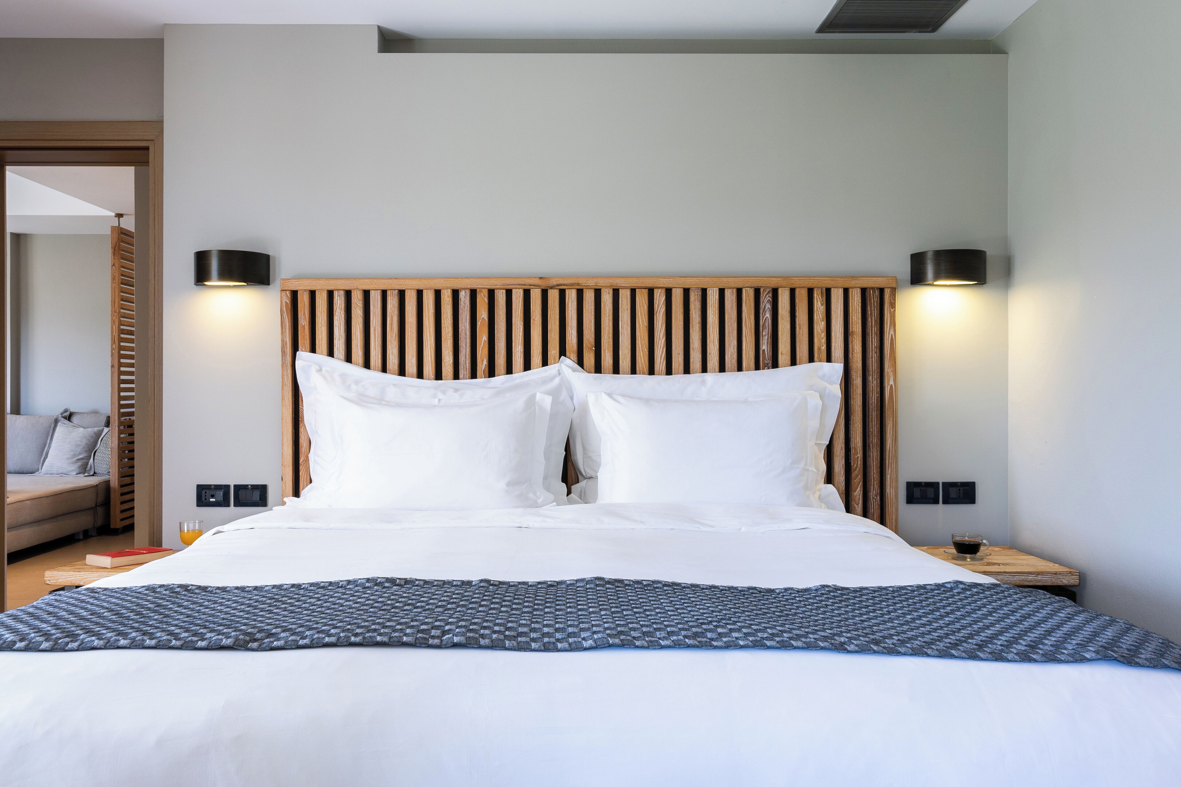 A neatly made bed with white linens, a wooden headboard, and two bedside lamps.