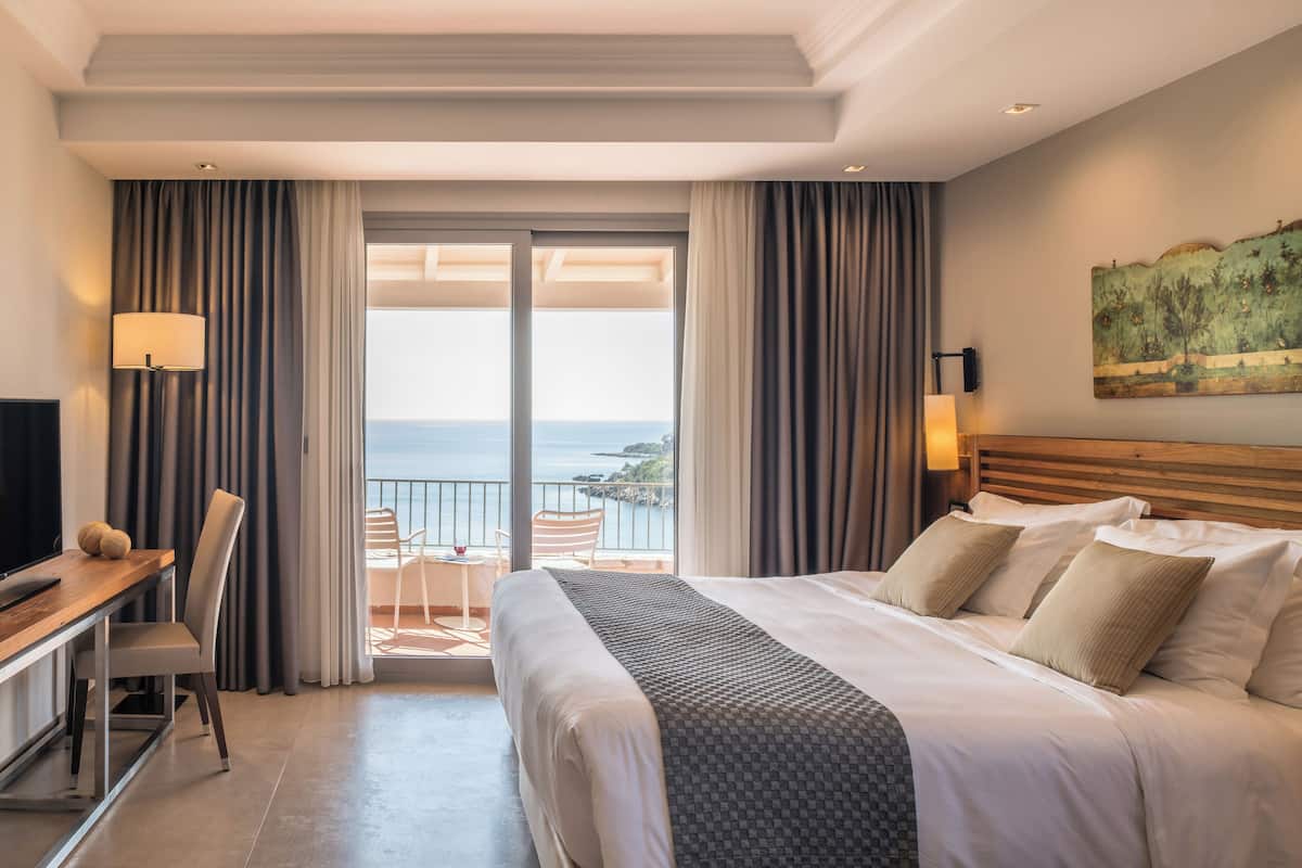 Hotelkamer met een bed, bureau, stoel, televisie en balkon met uitzicht op zee.