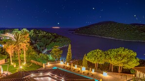 Une vue nocturne d’un complexe hôtelier avec une piscine, des palmiers et une vue sur la mer.
