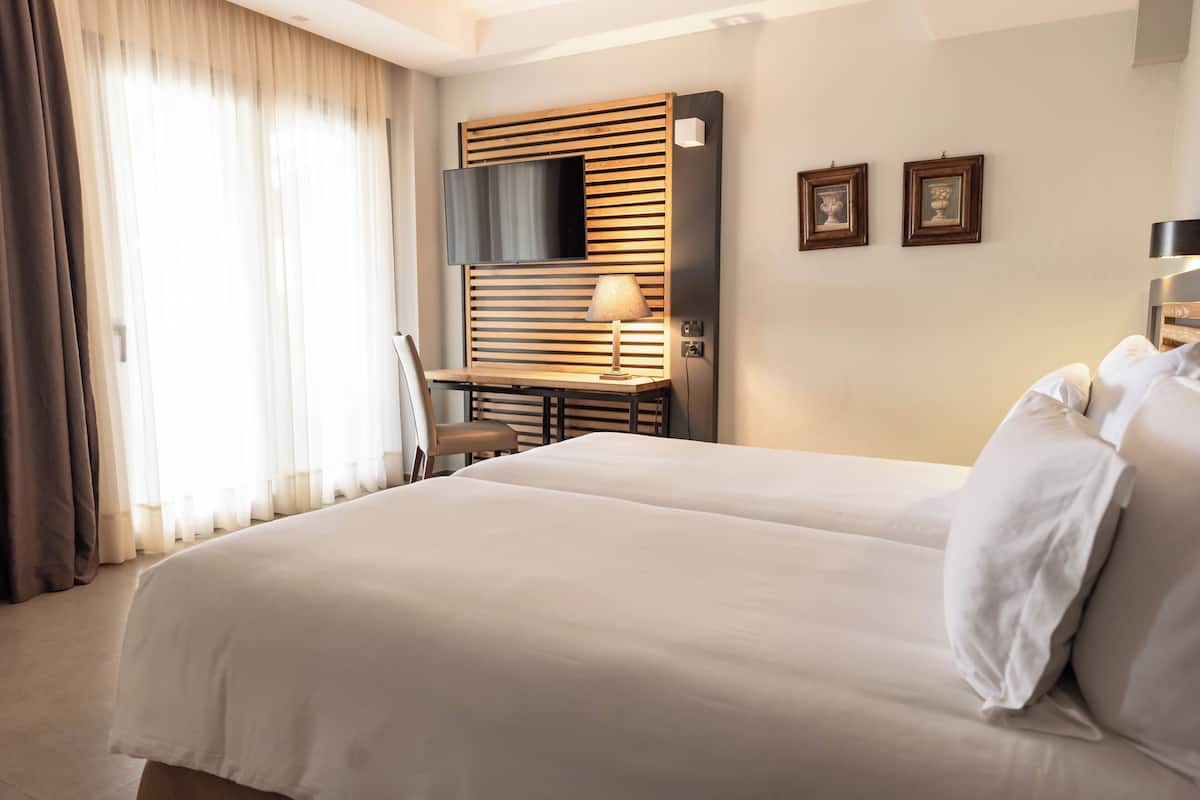 Een hotelkamer met een groot bed, een bureau met lamp, een aan een houten paneel bevestigde televisie, en twee ingelijste foto's aan de muur.