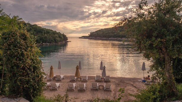 Une plage avec des chaises longues et des parasols, un sentier en pierre et une vue sur la mer.