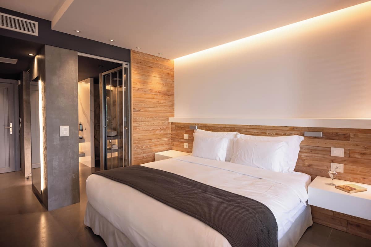 Een moderne hotelkamer met een groot bed, een houten hoofdeinde en een nachtkastje met een glas water.