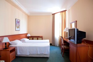 Een hotelkamer met twee bedden, een bureau met een televisie, een stoel en een lamp.