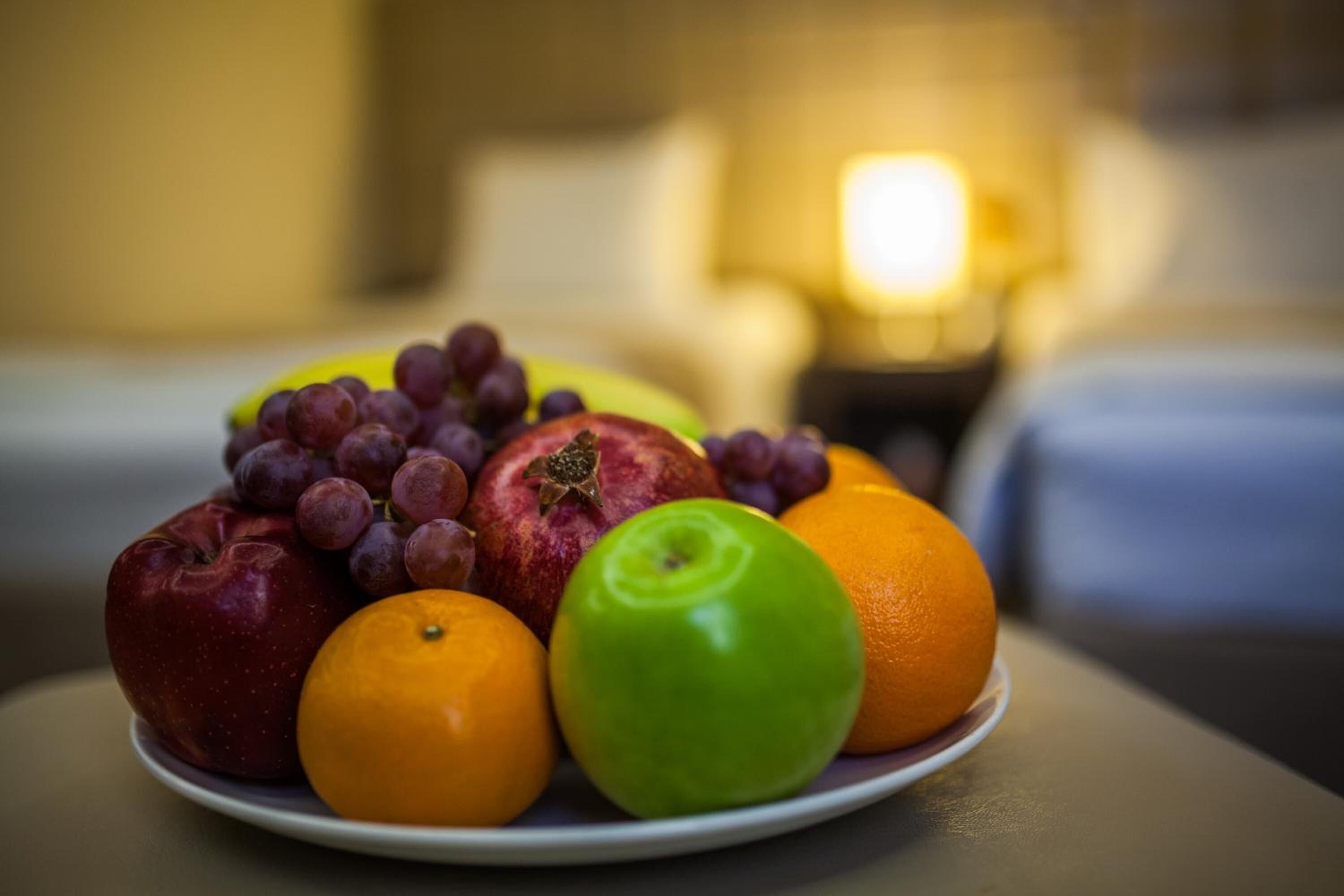 A plate of fruits including apples, grapes, oranges, and a pomegranate.