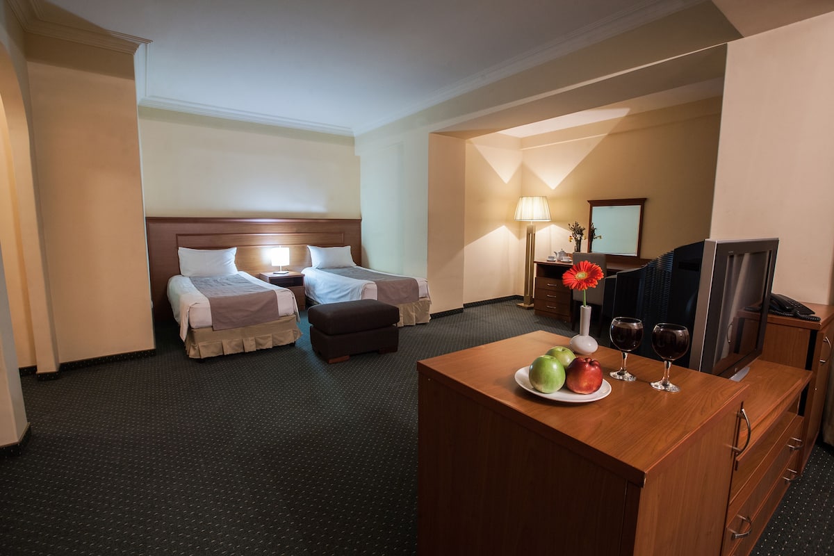 Una habitación de hotel con dos camas, un escritorio con televisor y una lámpara.