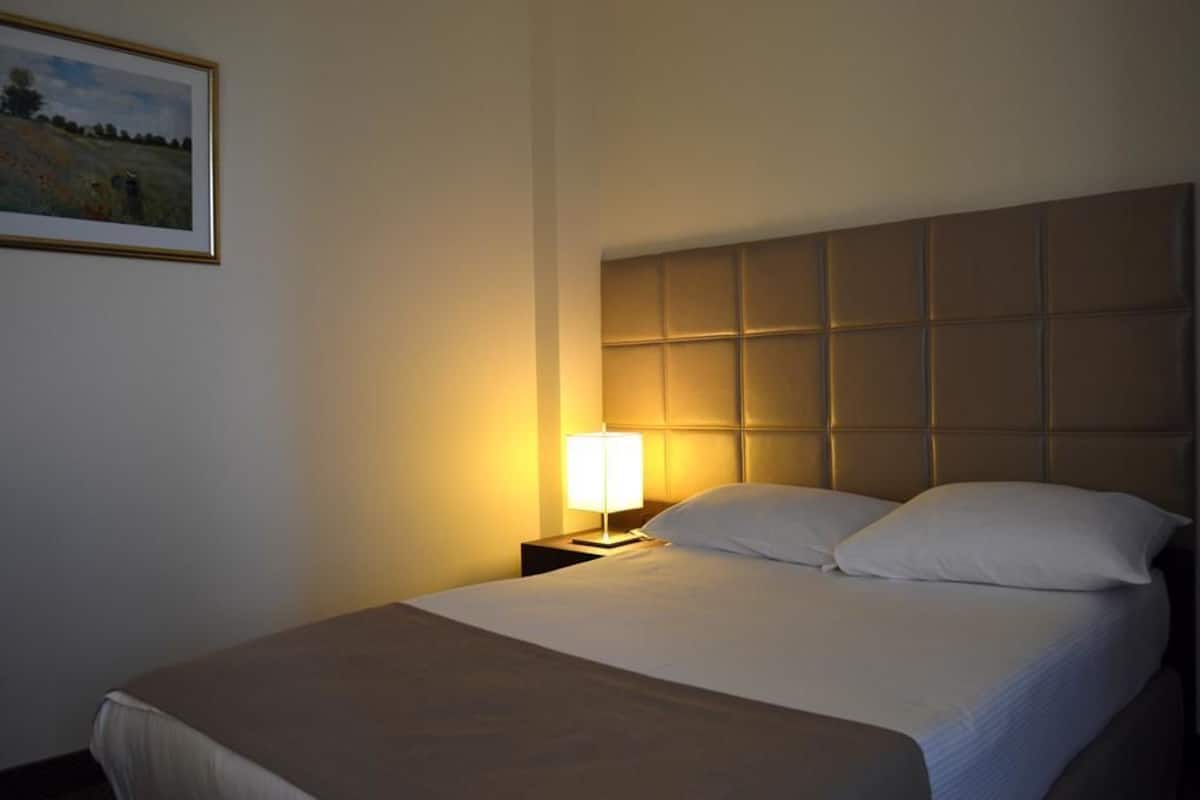 Una habitación de hotel con una cama grande, un cabecero de diseño acolchado, una lámpara de noche y un cuadro en la pared.