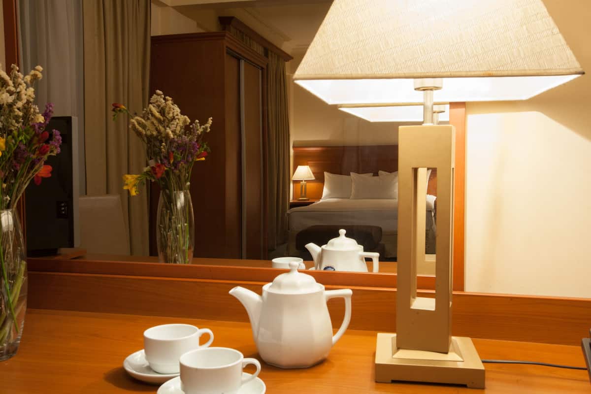 Una habitación de hotel con una mesa de madera, una tetera blanca, dos tazas y un jarrón con flores.