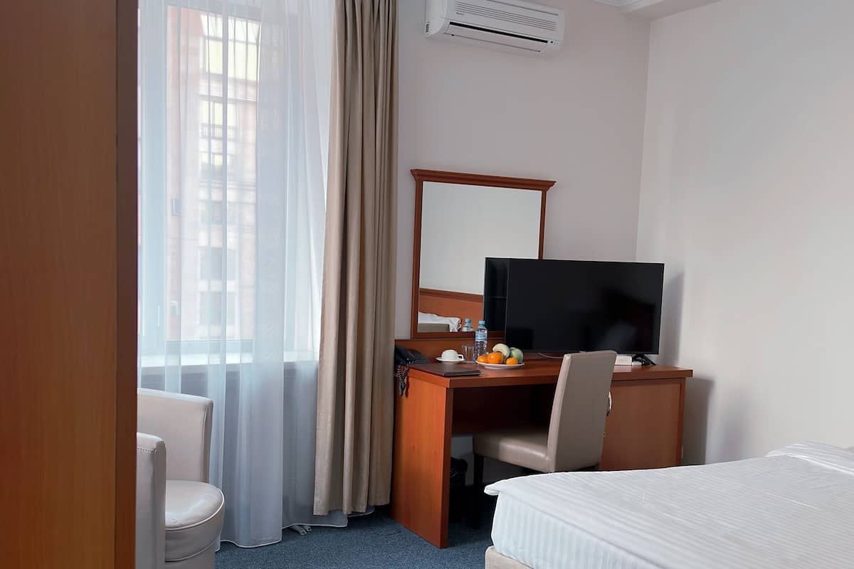 Habitación de hotel con cama, escritorio, computadora, silla, televisor y ventana con cortinas.