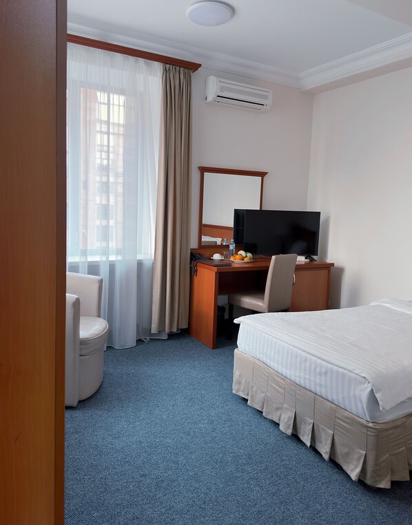 Une chambre d’hôtel avec un lit, un bureau équipé d’un ordinateur, une chaise, une télévision et une fenêtre avec des rideaux.